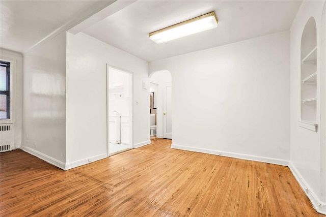 spare room with baseboards, arched walkways, radiator, and wood finished floors