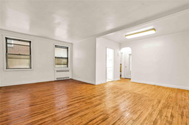 spare room with baseboards, arched walkways, radiator, and light wood finished floors