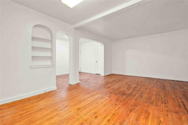 unfurnished room featuring built in features, arched walkways, baseboards, and wood-type flooring