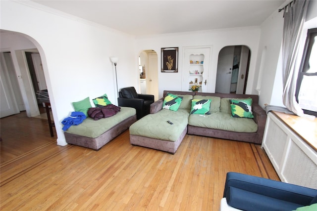 living room with crown molding, light wood-style floors, and arched walkways