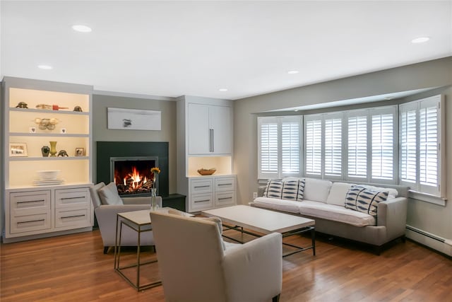 living room with recessed lighting, built in shelves, a warm lit fireplace, and wood finished floors