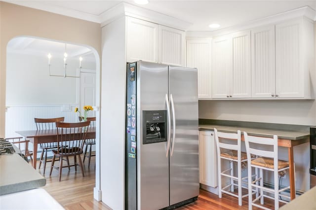 kitchen with light wood-style flooring, arched walkways, stainless steel fridge, and white cabinets