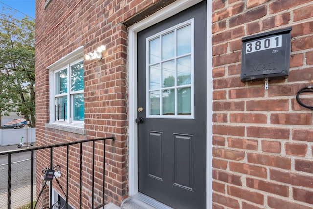 view of exterior entry featuring brick siding and fence