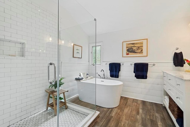 bathroom featuring a wainscoted wall, a stall shower, a freestanding bath, and wood finished floors