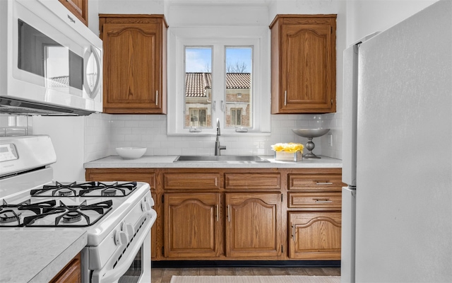 kitchen with brown cabinetry, white appliances, light countertops, and a sink