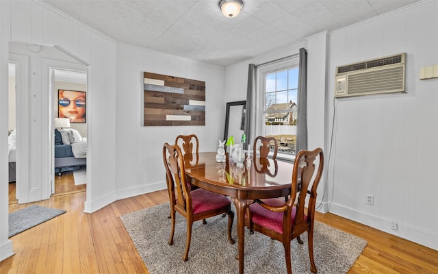 dining space featuring an AC wall unit, light wood-type flooring, baseboards, and ornamental molding