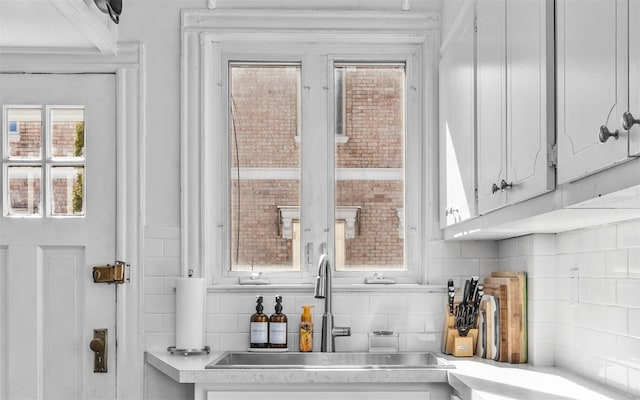 interior space featuring a sink, decorative backsplash, white cabinets, and light countertops