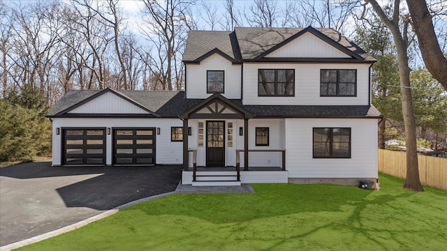 view of front of home with driveway, fence, roof with shingles, a front yard, and an attached garage