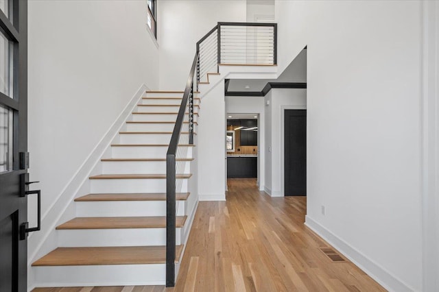 stairs with visible vents, a high ceiling, baseboards, and wood finished floors