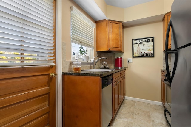 kitchen with freestanding refrigerator, a sink, dishwasher, brown cabinets, and backsplash