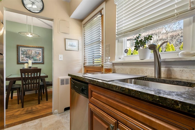 kitchen with dark stone countertops, dishwasher, radiator, and a sink