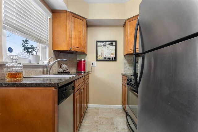 kitchen featuring brown cabinetry, baseboards, a sink, stainless steel appliances, and tasteful backsplash