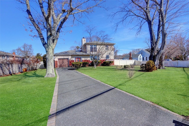 traditional-style home featuring an attached garage, a chimney, a front yard, and fence