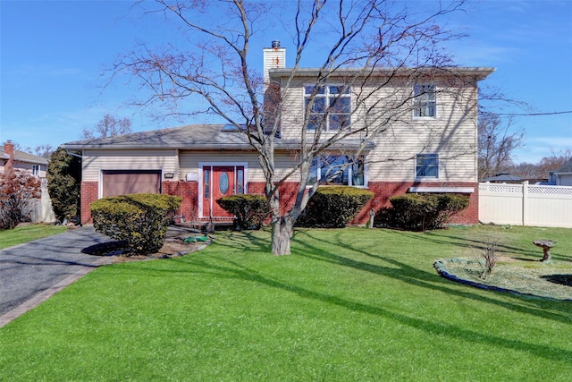 traditional home featuring brick siding, fence, a front yard, a chimney, and driveway