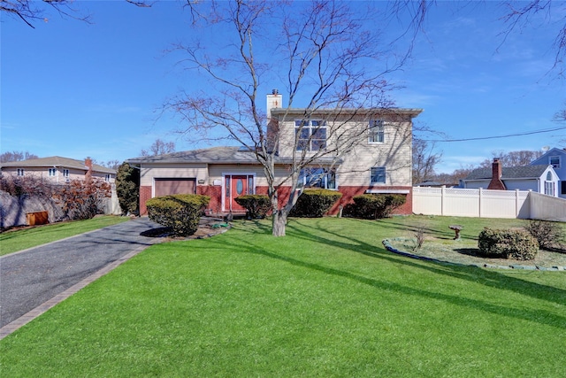 view of front facade with a front yard, fence, driveway, a chimney, and brick siding