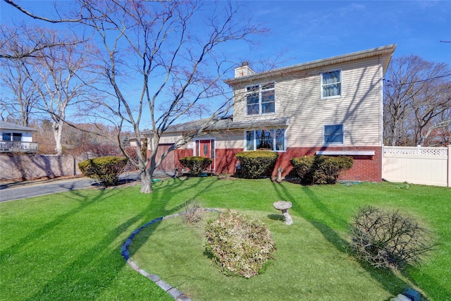 rear view of property with brick siding, a lawn, a chimney, and fence