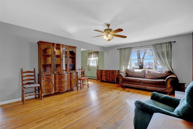 living room featuring light wood-type flooring, baseboards, baseboard heating, and a ceiling fan