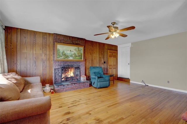 living area with a ceiling fan, baseboards, light wood finished floors, wood walls, and a brick fireplace