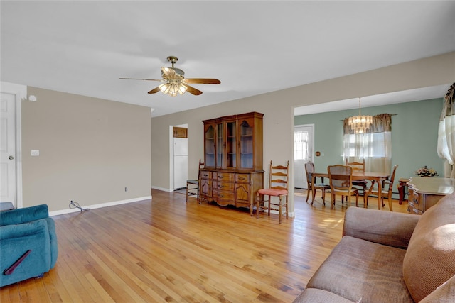 living room with ceiling fan with notable chandelier, light wood-type flooring, baseboard heating, and baseboards