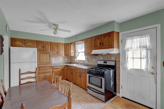 kitchen with stainless steel gas range oven, under cabinet range hood, decorative backsplash, freestanding refrigerator, and a sink