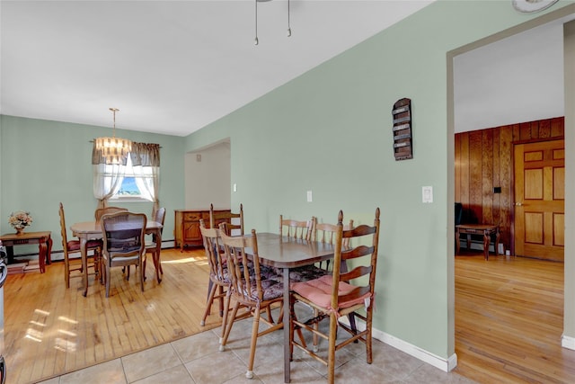 dining room featuring light wood-type flooring, baseboards, a notable chandelier, and wooden walls