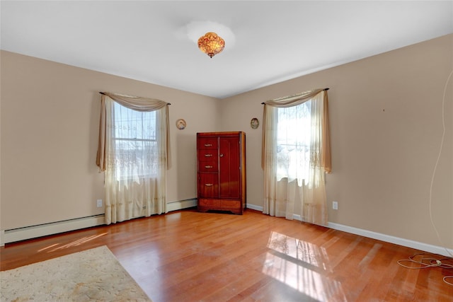 spare room with a baseboard heating unit, baseboards, and wood finished floors