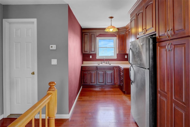 kitchen featuring wood finished floors, baseboards, freestanding refrigerator, a sink, and light countertops