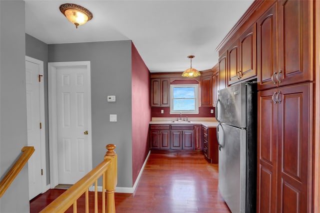 kitchen with baseboards, dark wood finished floors, freestanding refrigerator, a sink, and light countertops