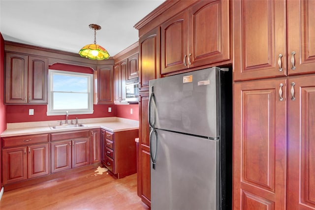 kitchen featuring light countertops, light wood-style flooring, appliances with stainless steel finishes, hanging light fixtures, and a sink