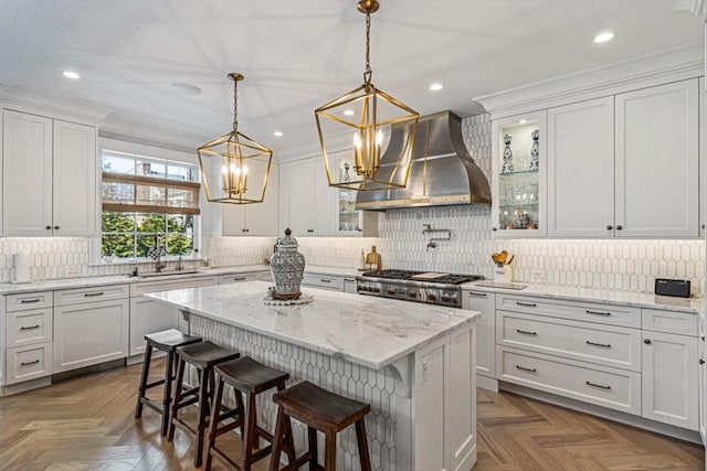 kitchen featuring a sink, white cabinets, a kitchen breakfast bar, wall chimney exhaust hood, and range