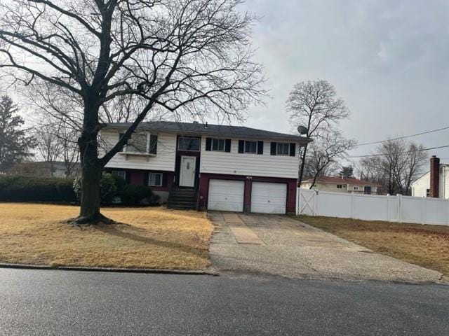 bi-level home with concrete driveway, an attached garage, and fence