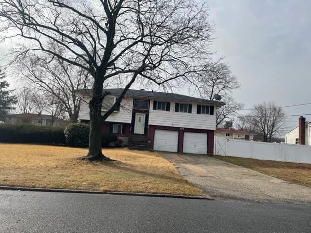 split foyer home with concrete driveway, an attached garage, and fence