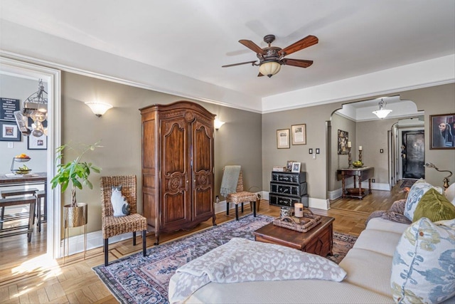 living area with arched walkways, baseboards, and ceiling fan