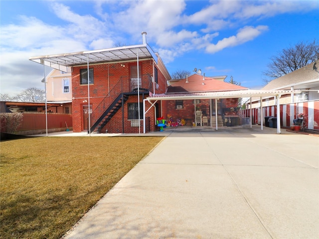 back of house featuring stairway, a yard, fence, and brick siding