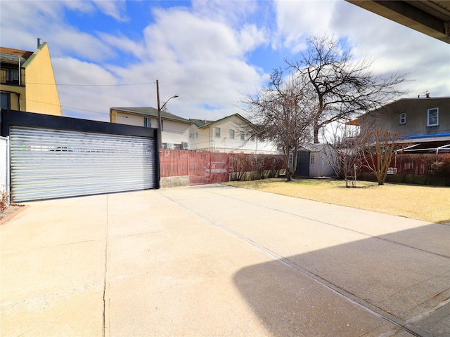 view of patio with an outdoor structure, concrete driveway, and fence