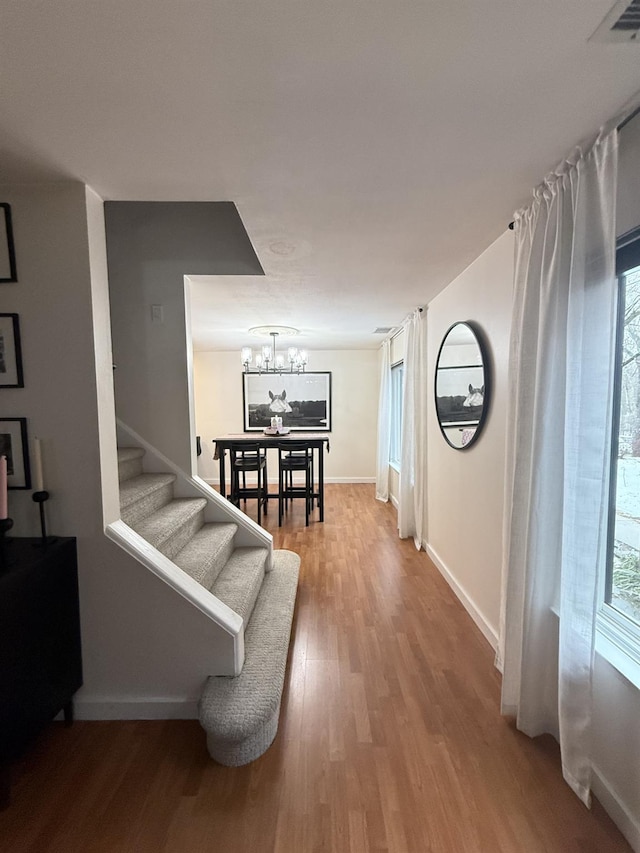 hallway featuring stairway, a notable chandelier, wood finished floors, and plenty of natural light