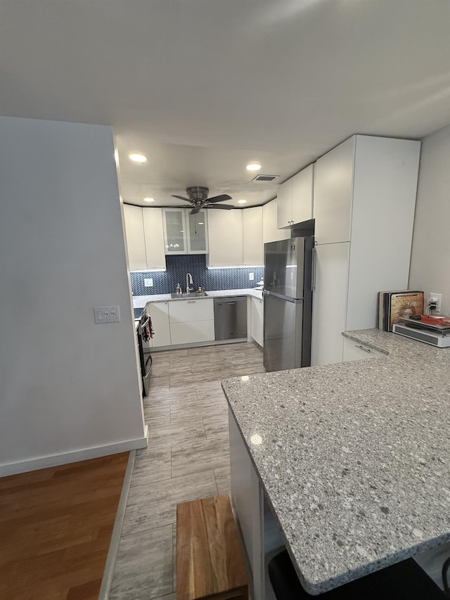 kitchen featuring light stone countertops, visible vents, stainless steel appliances, white cabinets, and backsplash