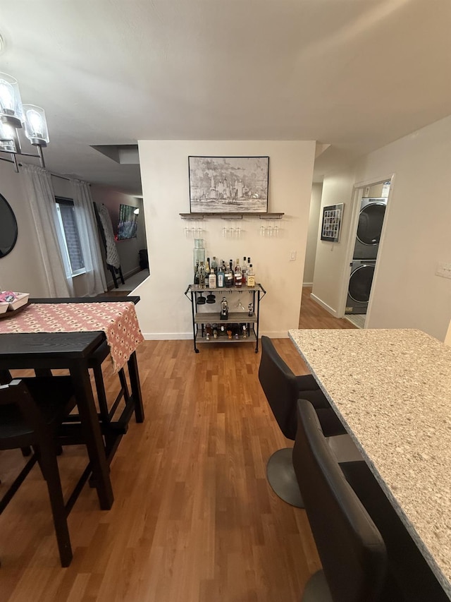 dining area featuring stacked washer / drying machine, baseboards, and wood finished floors