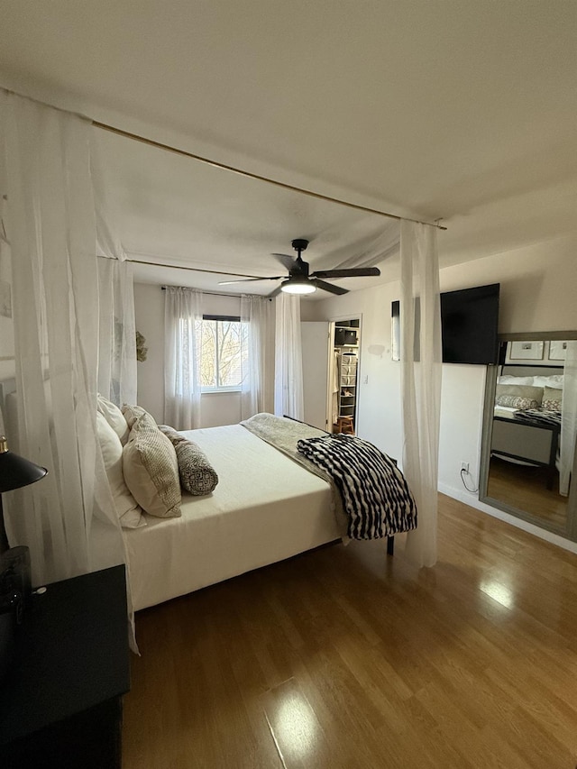 bedroom with a walk in closet, wood finished floors, and ceiling fan