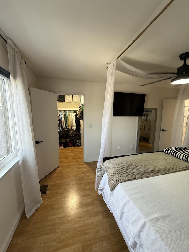 bedroom with a walk in closet, wood finished floors, visible vents, and baseboards