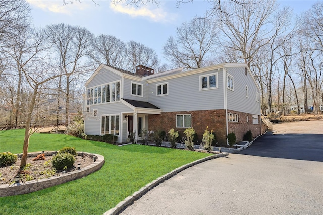 view of front of property featuring a front yard, brick siding, a chimney, and driveway