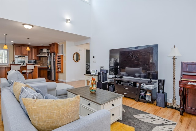 living room with baseboards, light wood-style floors, and a towering ceiling