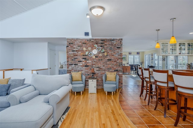 living room featuring light wood-style floors, brick wall, and vaulted ceiling