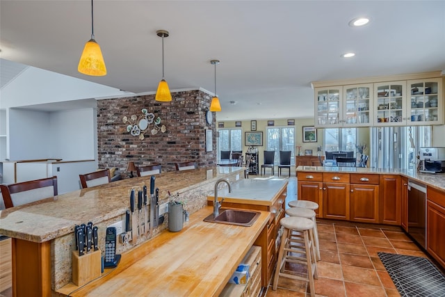 kitchen with a breakfast bar area, a sink, hanging light fixtures, stainless steel dishwasher, and brown cabinets