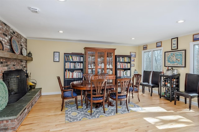 dining area featuring baseboards, ornamental molding, recessed lighting, light wood-style flooring, and a fireplace