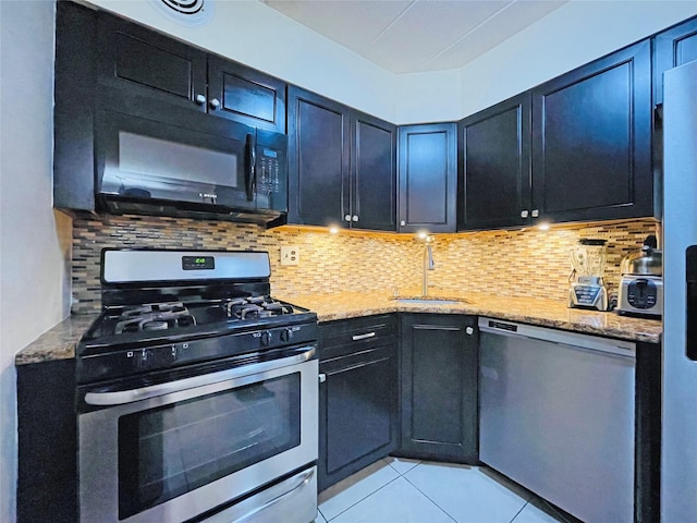 kitchen with a sink, light stone counters, backsplash, dark cabinetry, and appliances with stainless steel finishes