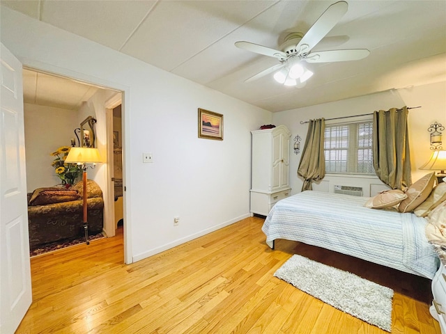 bedroom with a ceiling fan, baseboards, light wood-type flooring, and a wall mounted air conditioner