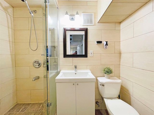 bathroom with visible vents, a shower stall, toilet, vanity, and tile walls