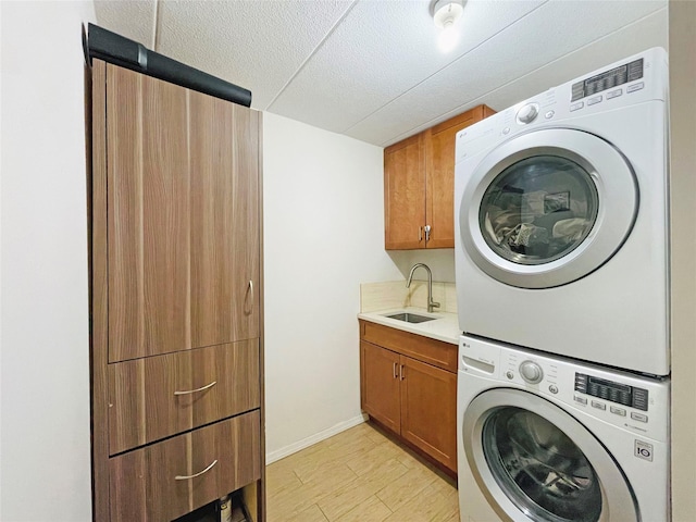 washroom featuring stacked washer / dryer, light wood-type flooring, cabinet space, a textured ceiling, and a sink