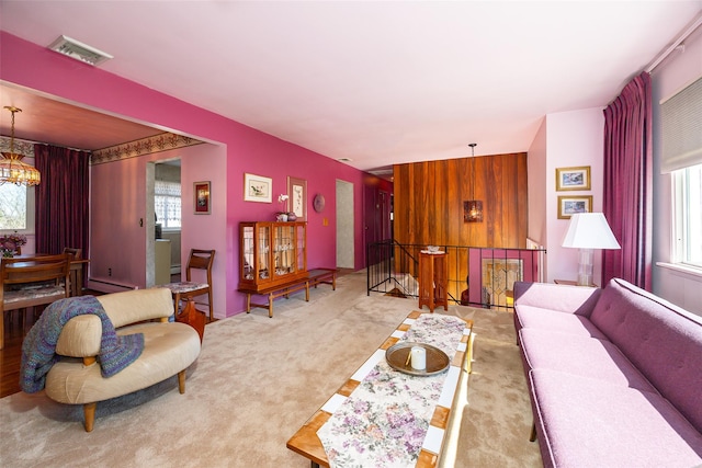 living area with visible vents, carpet, a chandelier, and wood walls